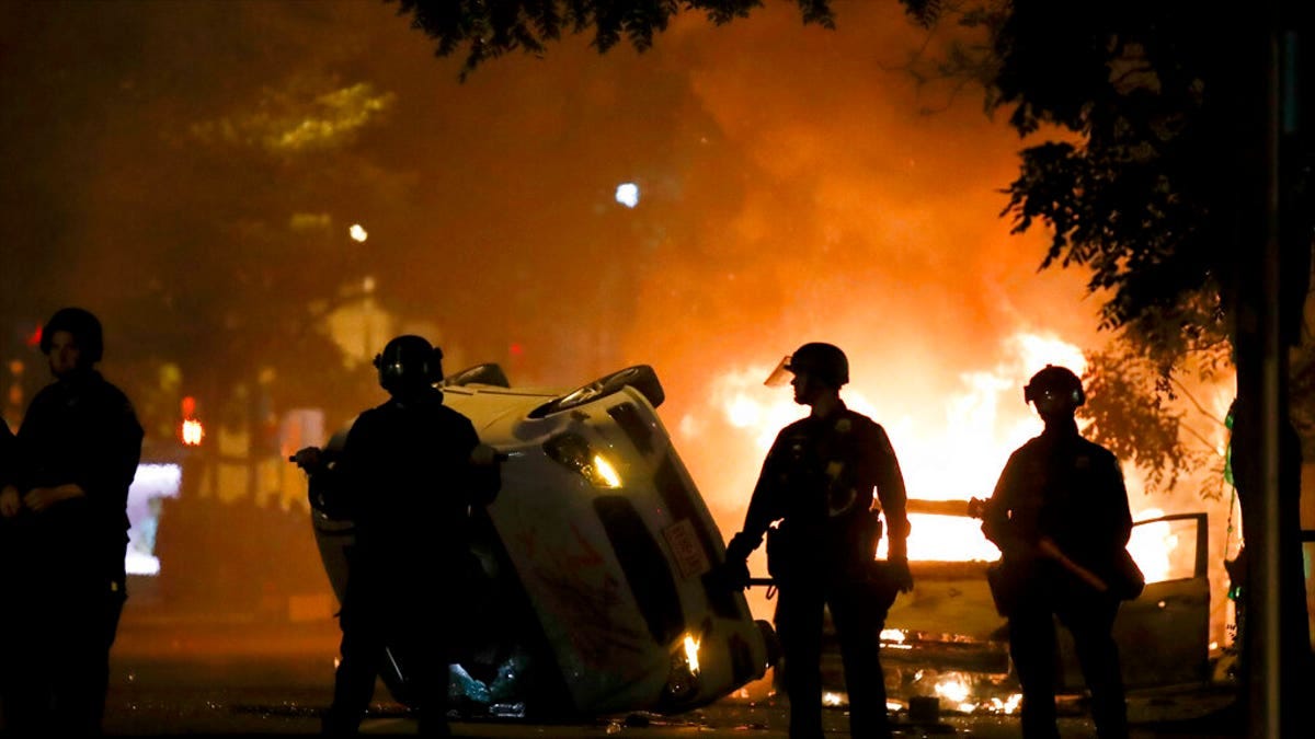 Police stand near a overturned vehicle and a fire as demonstrators protest the death of George Floyd, Sunday, May 31, 2020, near the White House in Washington. Floyd died after being restrained by Minneapolis police officers. (AP Photo/Alex Brandon)