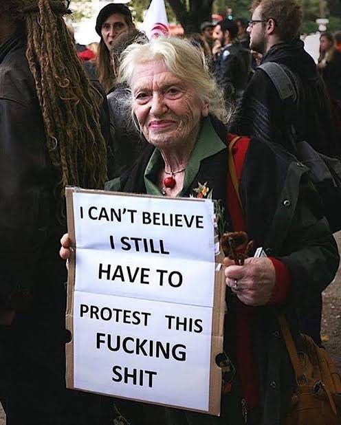 descrição da imagem: uma mulher idosa segurando um cartaz que diz:"I can't believe I still have to protest this fucking shit", que significa: "eu não acredito que ainda tenho de protestar por essa merda". 