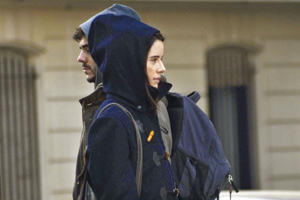 cena do filme "medianeras" um homem e uma mulher se cruzam na rua mas não se olham. ela usa um casaco azul escuro e ele uma jaqueta marrom. ambos estão com a cabeça coberta por um capuz.