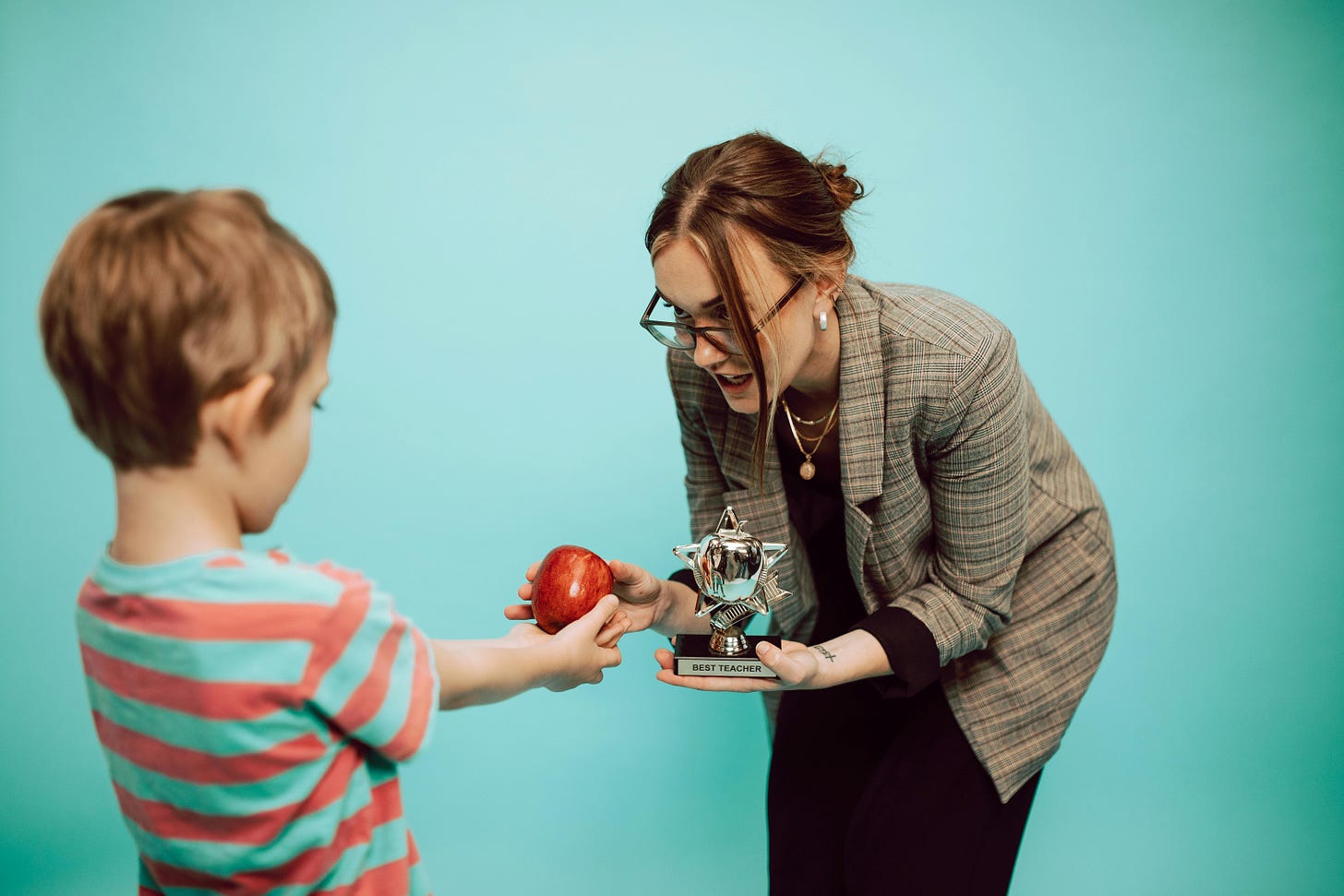 A teacher giving a student an award and an apple. es