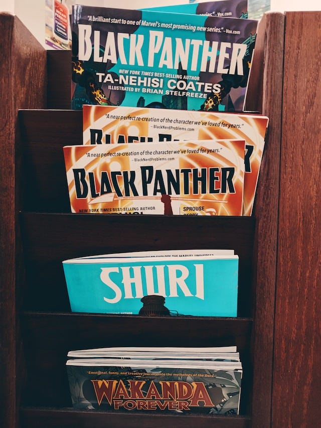 a black vertical magazine rack full of Black Panther and Shuri comics, that are alternately blue and orange in color scheme.