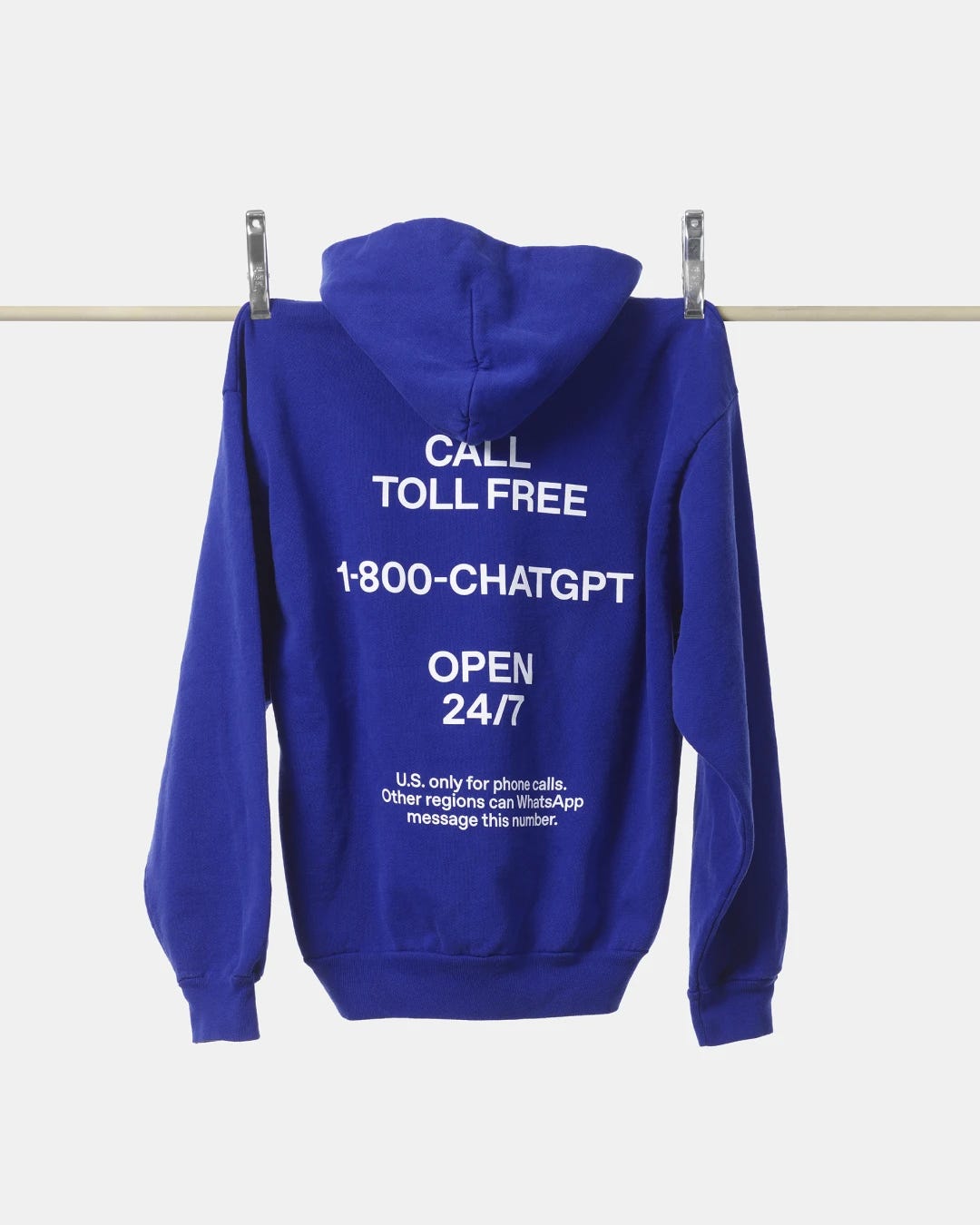 A blue hoodie hanging on a wooden rod against a plain white background. The back reads in white text: “CALL TOLL FREE 1-800-CHATGPT OPEN 24/7,” promoting availability.