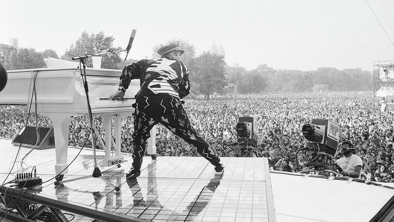 Elton John performing on piano in Central Park, New York. 