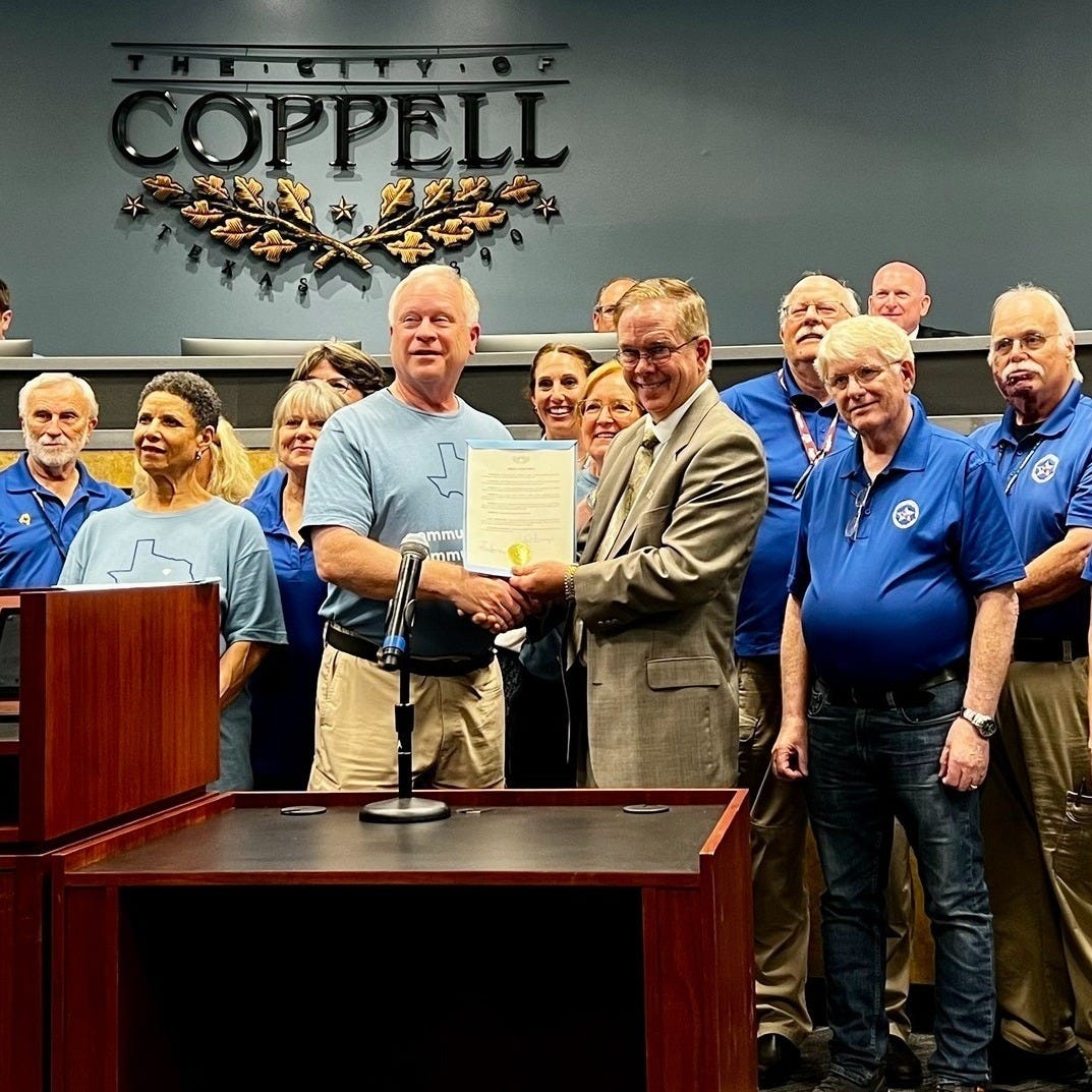 Two gentlemen shake hands while flanked by volunteers in blue shirts