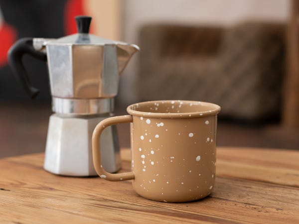 Moka pot with brown coffee mug on wooden surface