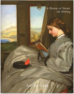 A woman in a gray dress sits reading by a window.