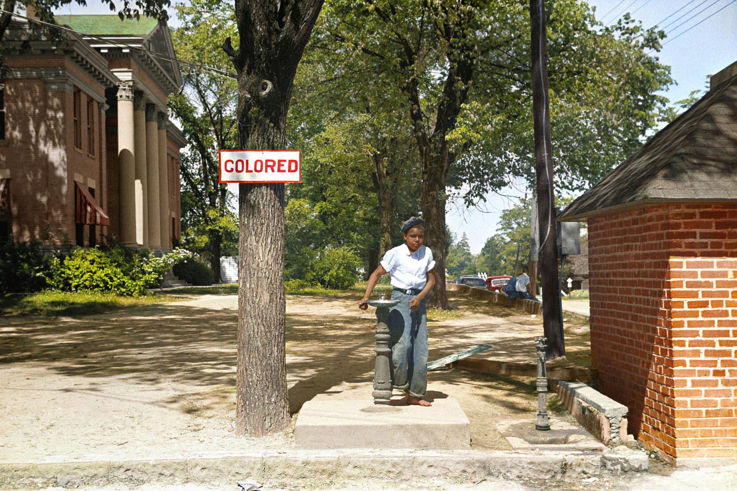A black boy at a segregated drinking fountain with a sign that reads "colored" nearby