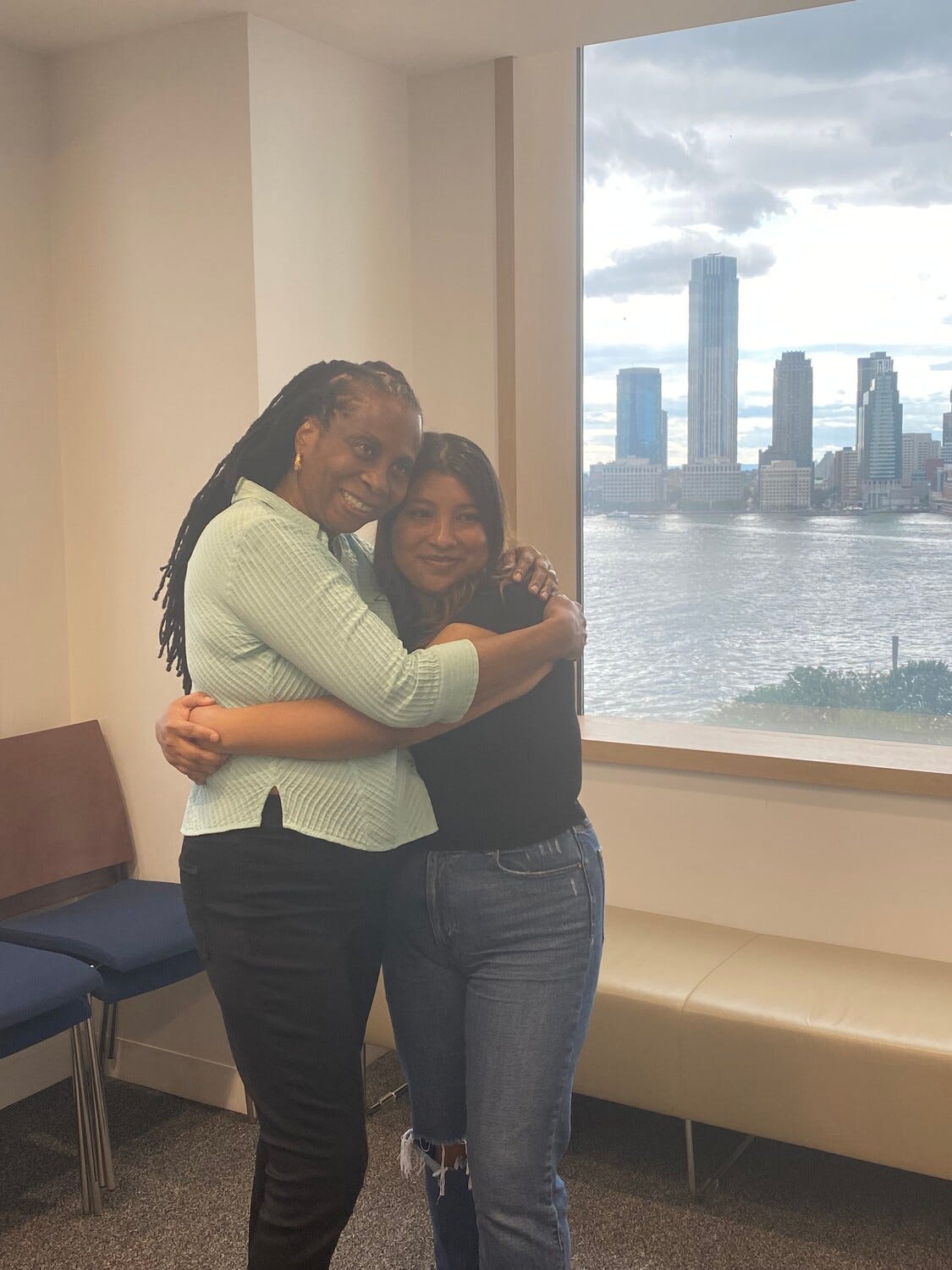 Brenda embracing her mentee Dolores in front of a window featuring the skyline