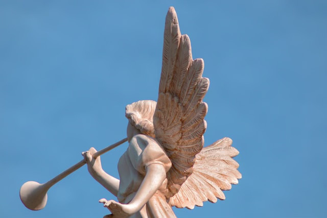 a statue of an angel blowing on a horn against a blue sky