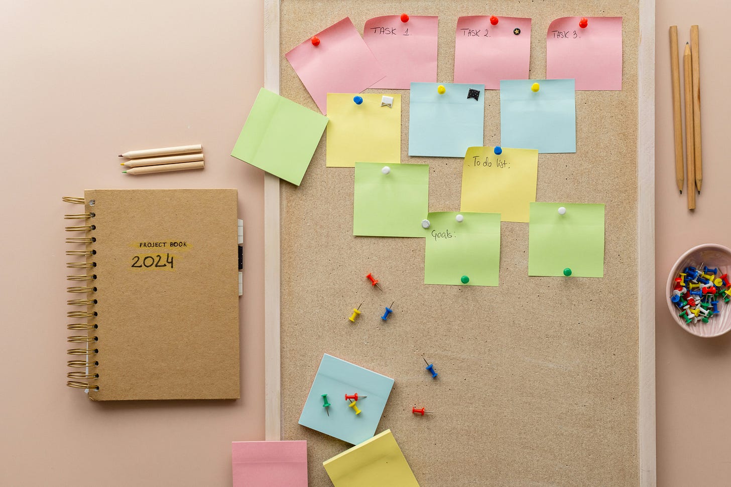 corkboard with post-it notes pinned to it by notebook and pencils