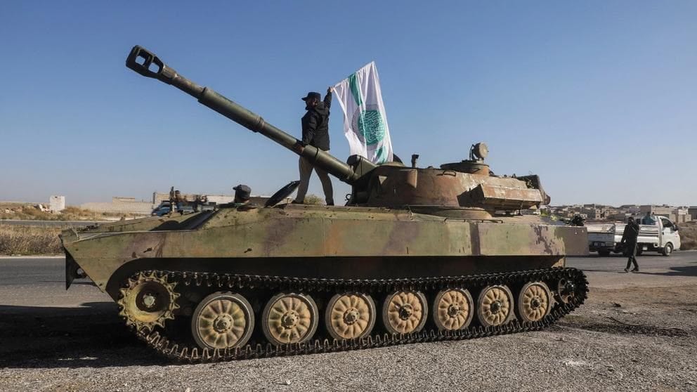 Um combatente rebelde em cima de um veículo militar enquanto carrega uma bandeira Hayat Tahrir al-Sham na cidade de Saraqeb, no noroeste da província de Idlib, Síria, em 1º de dezembro de 2024.