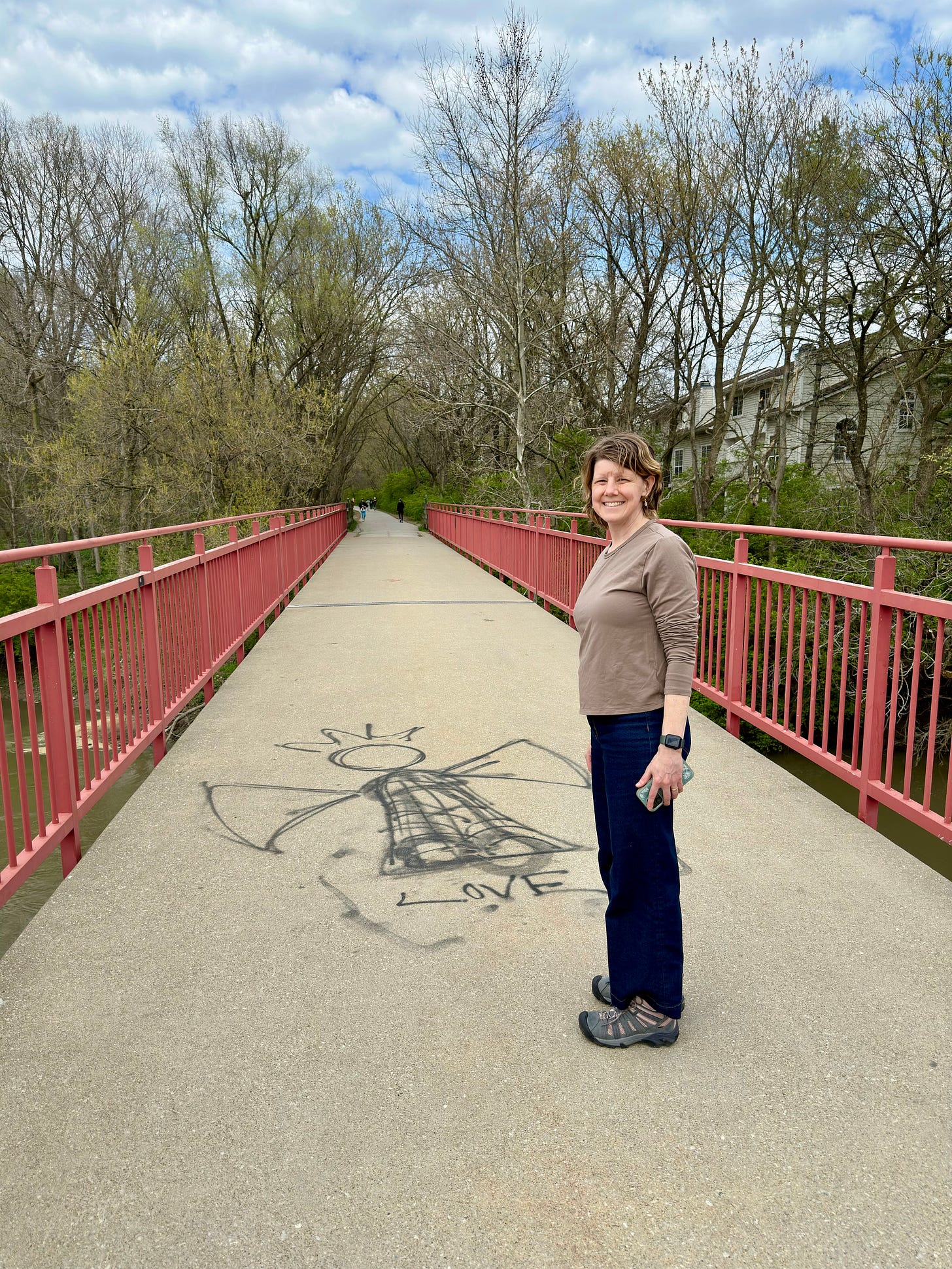 Heidi standing on a paved bike trail in front of an angel graffiti painted in black on the cement at her feet.