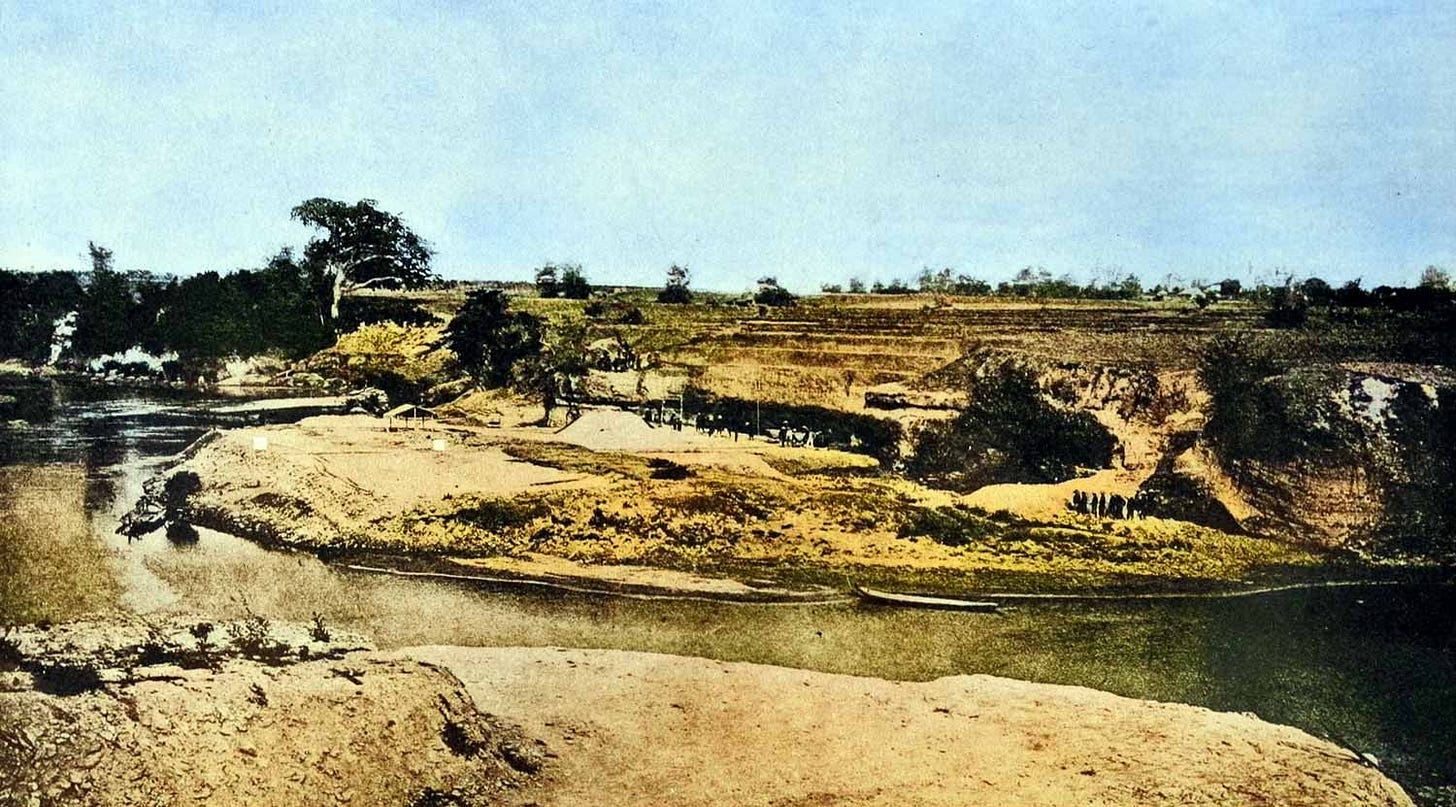 A photo from a distance showing large river terrace excavation and river flowing in front.