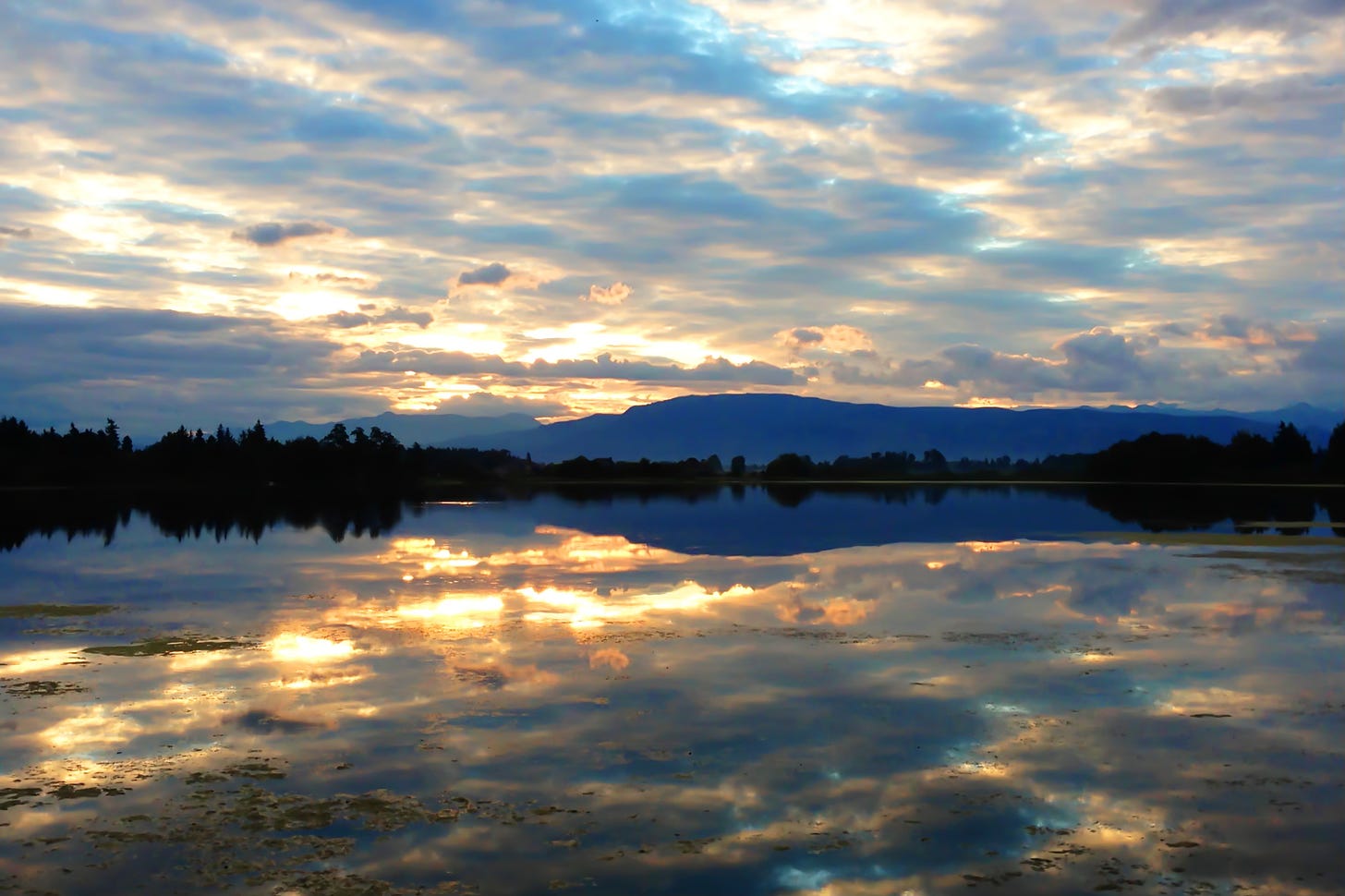 The sunrises over a mountain lake, weaving gold through clouds and reflections.