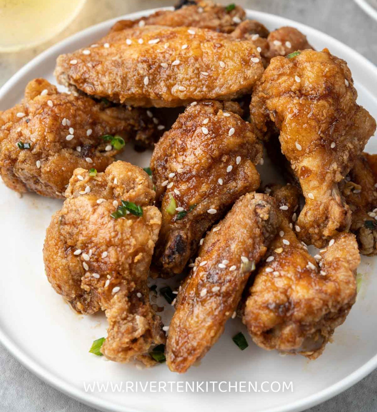 A plate full of delicious crispy sweet/salty fried chicken wings sprinkled with sesame seeds and scallions. 