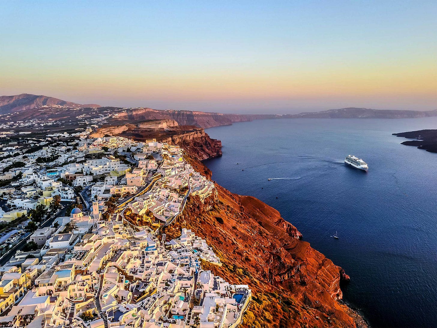 Aerial view of Santorini with cruise ship passing by on the water.