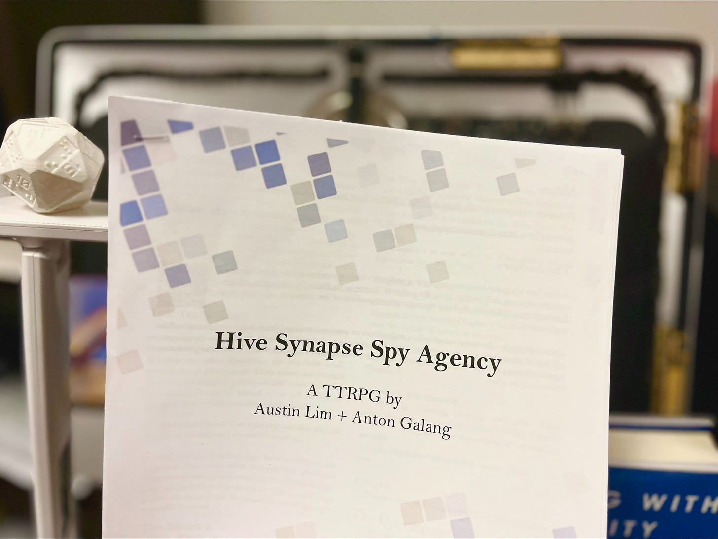 Image contains the cover of the game Hive Synapse Spy - A TTRPG by Austin Lim + Anton Galang. On the left of the paper sits a 3D printed braille 20-sided die, on the right a corner of the book Playing with Reality by Kelly Clancy, and behind it a blurred image of the circuits of a mac computer.