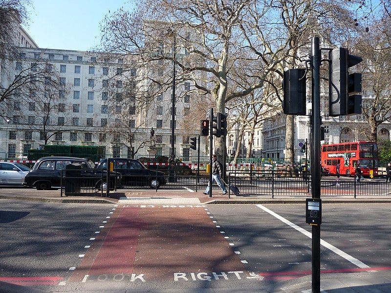 A pedestrian crossing, with guard rails, across Victoria Embankment in London. It is a sunny day, and the road is busy with traffic