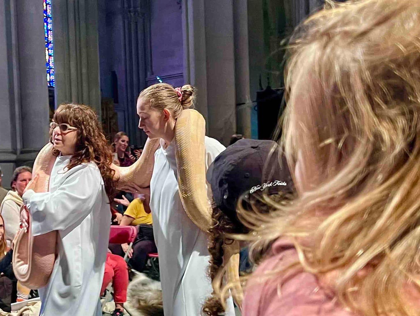 Fjora Markides looking on at two women carrying a boa constrictor in the 2023 Blessing of the Animals procession at St. John the Divine in NYC