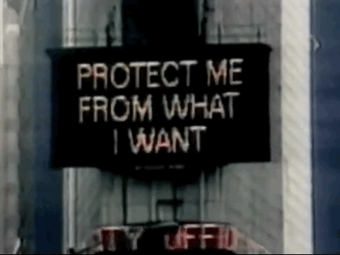 Jenny Holzer's "Protect Me from What I Want" flashes on an construction sign attached to an exterior wall