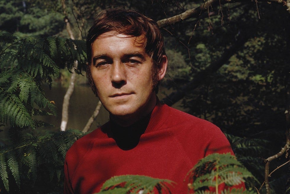 Michael Jayston As Frederick Royce standing behind a bush in a red top
