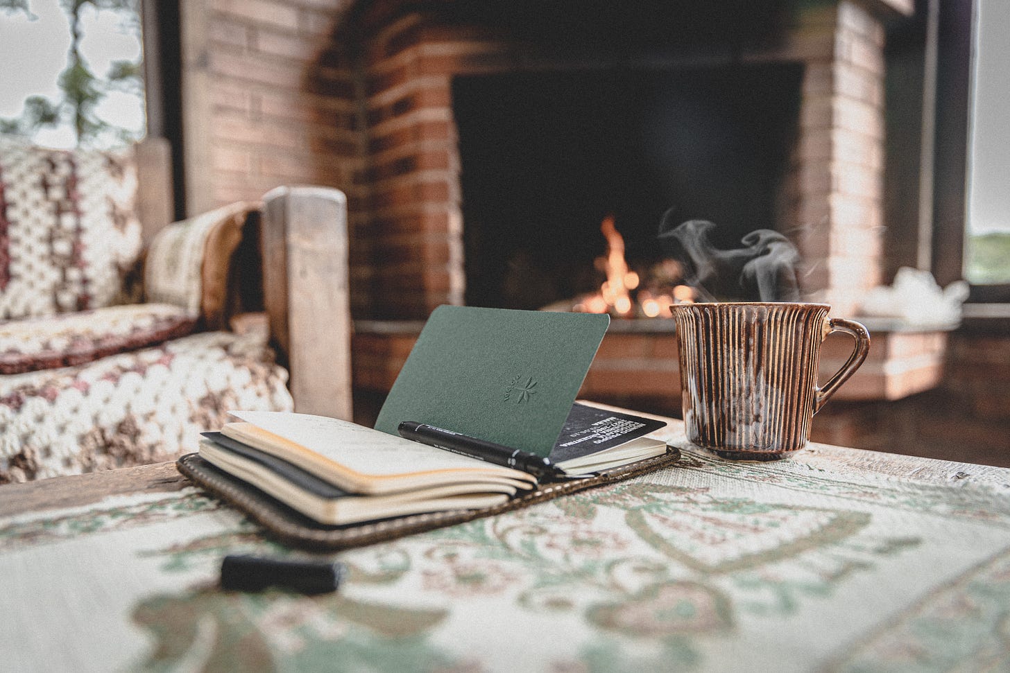 notebook on table by mug in front of chair and fireplace
