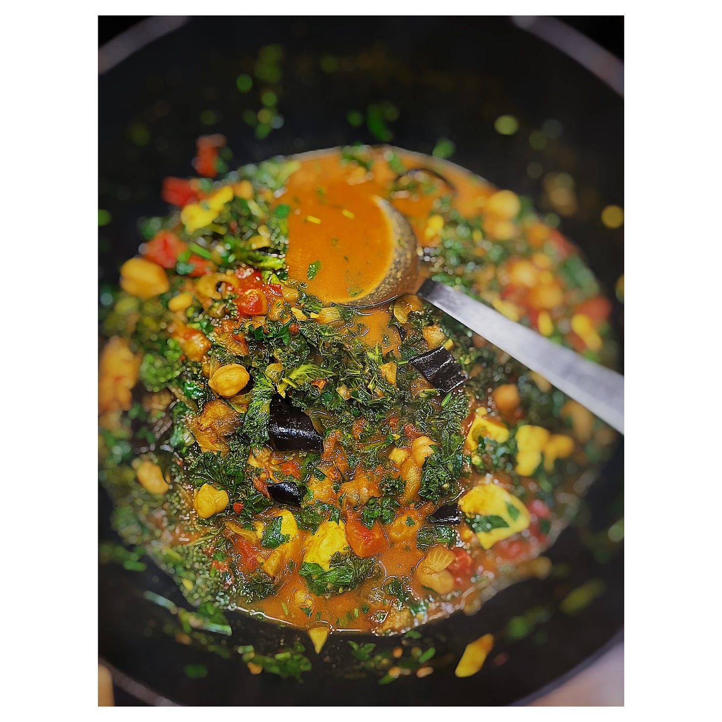 A close up overhead photo of a black wok with some curry cooking and a large serving spoon sticking out
