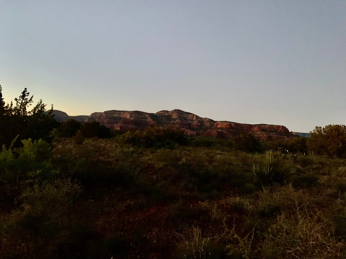 Twilight over marbled cliffs and, the outline of juniper bushes in the foreground