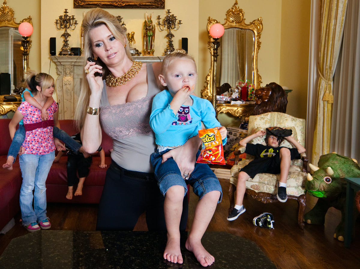 Jackie Siegel on the phone carrying a child on her hip, with several of her other children in the background