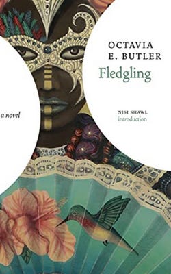 Book cover of Fledgling by Octavia Butler, with an image of a Black face covered by an ornate mask, holding a fan printed with the image of a hummingbird at a flower.