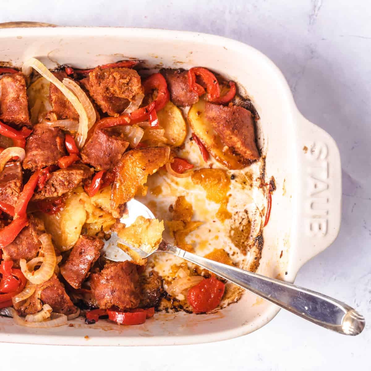 Potatoes and sausage casserole in baking dish with serving spoon.
