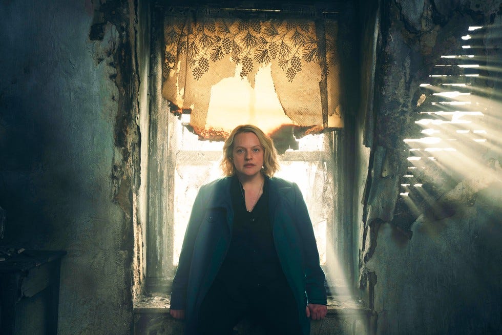 Elisabeth Moss as June, leaning on a windowsill in a derelict room