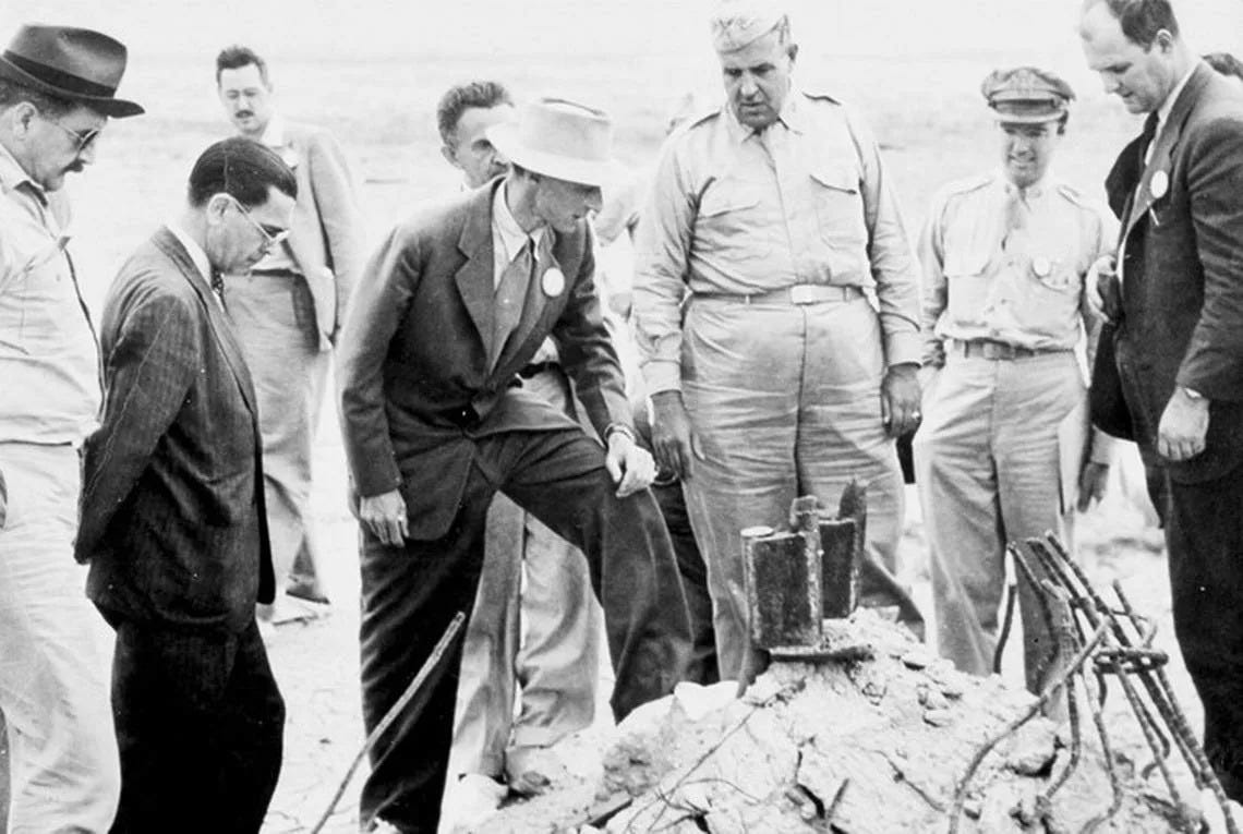 Oppenheimer and Gen. Groves at the Trinity detonation site, where the first atomic bomb was tested in 1945. Black and white photo.