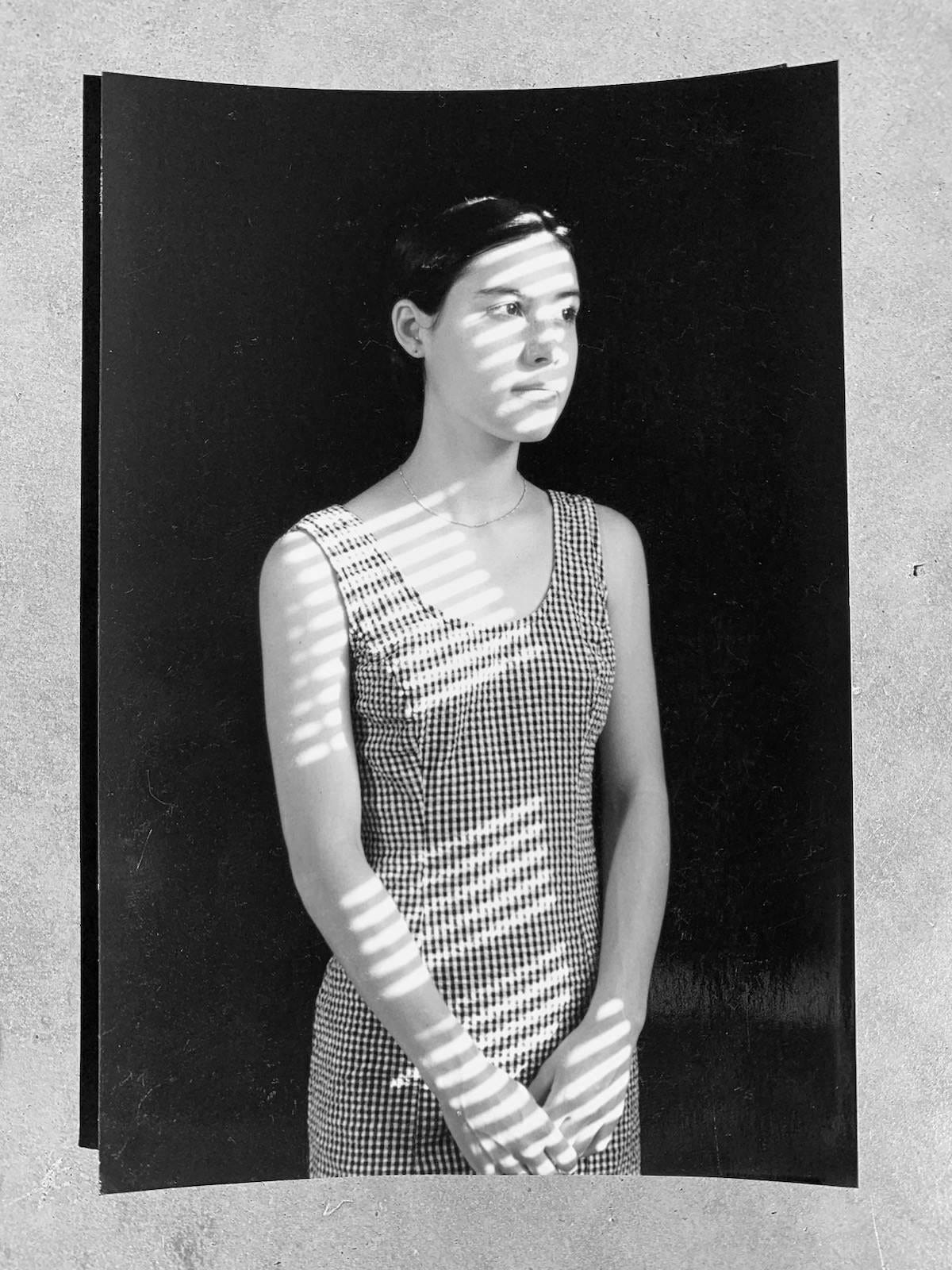 Author as a young girl in her early 20s wearing a black and white dress with sunlight streaming through blinds black and white