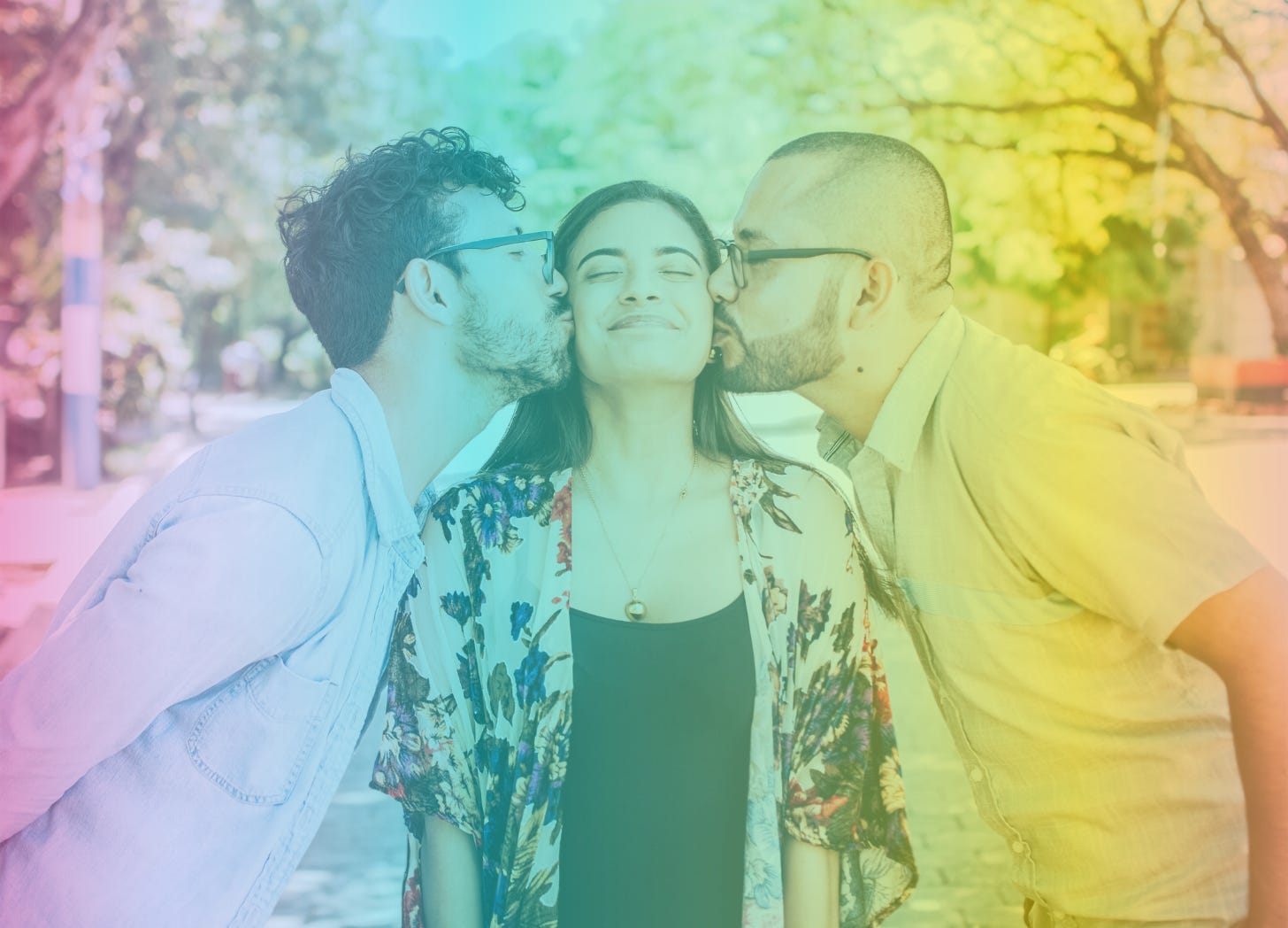 A rainbow-filtered photo of a femme-presenting person with olive skin smiling and closing her eyes as two men—one on either side of her—kisses her cheeks dotingly.
