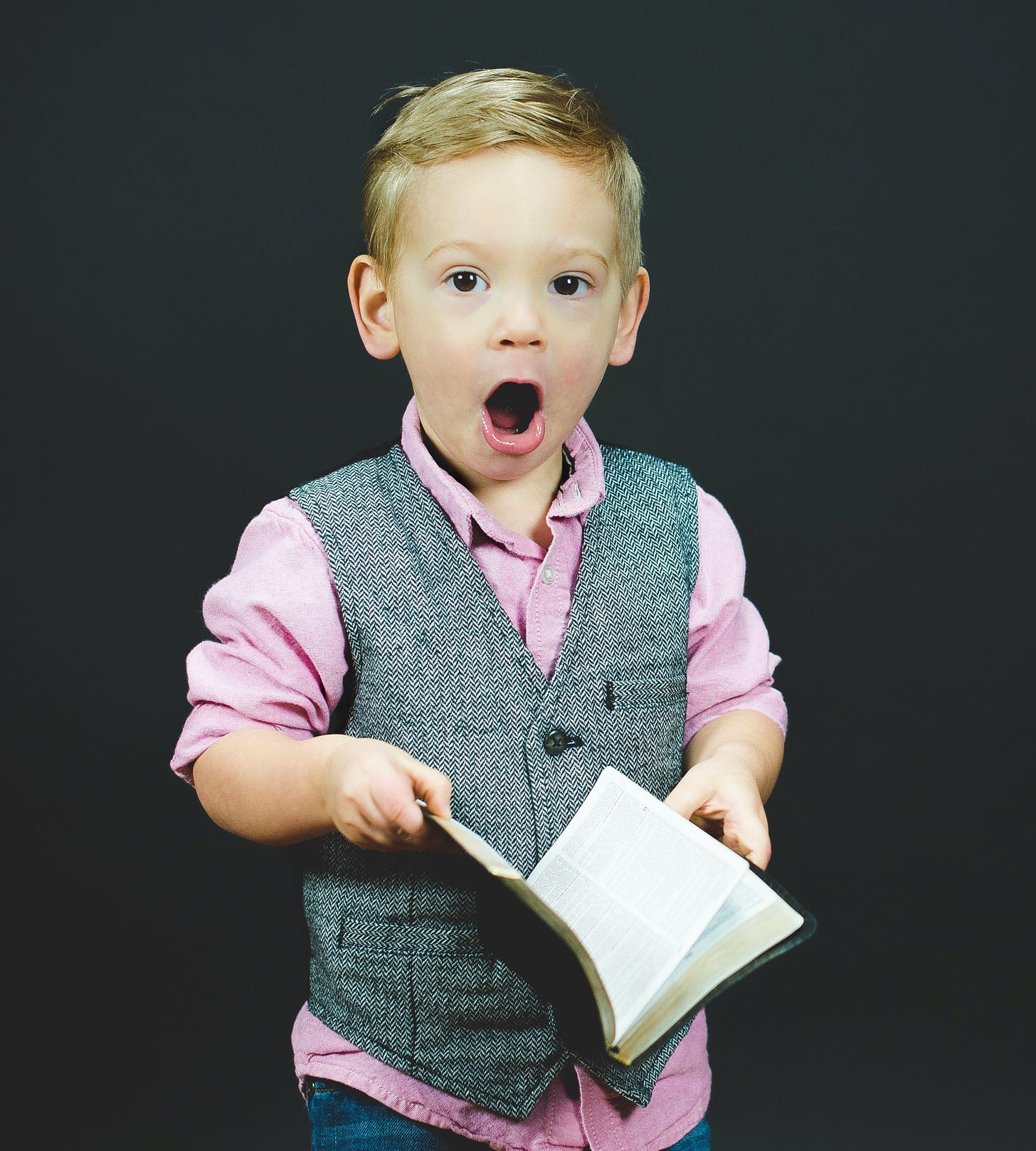 Young boy holding an open book (possibly a Bible) and looking at camera with an open-mounted expression of surprise