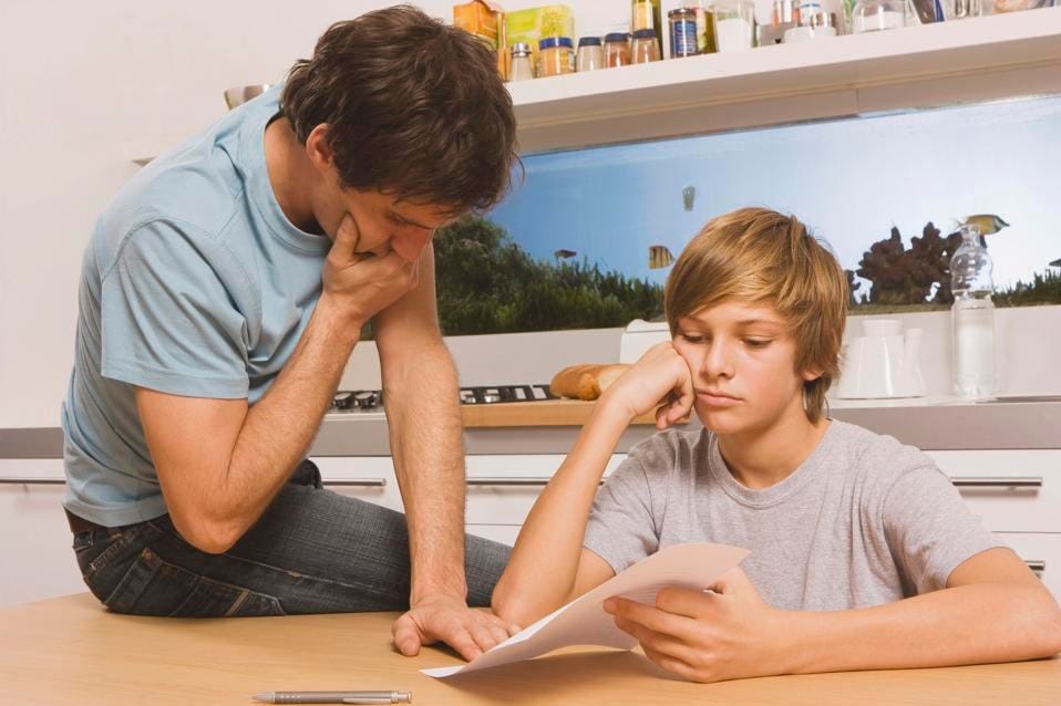 Father and son (13-14) looking at report card, hands to chin