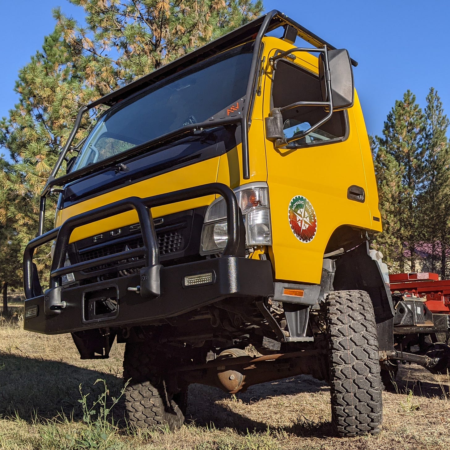 the same work truck, but now a bright yellow with all the tape and plastic off and the trim pieces put back on--very nice looking against a blue sky and green pine trees in the background