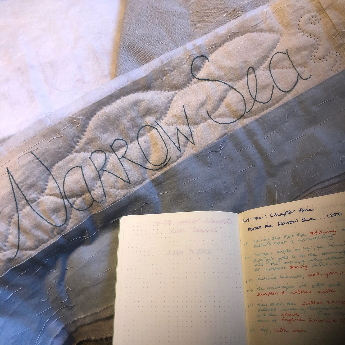 Quilted piece with the words “Narrow Sea” embroidered. Waves and an eel quilted in the background. A notebook in the foreground.
