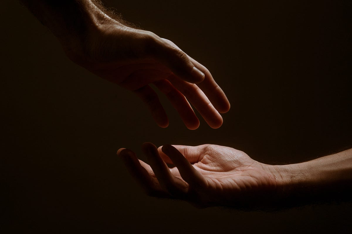 dark background with two illuminated hands reaching for each other