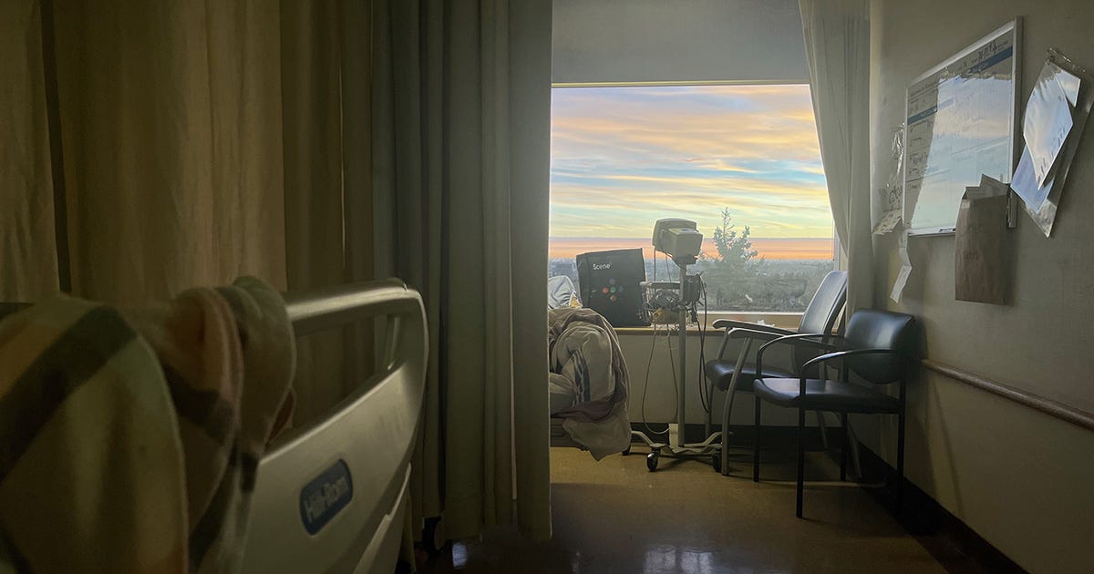 Darkened hospital room with a beautiful sunrise with cloud streaks in pink and pale blue