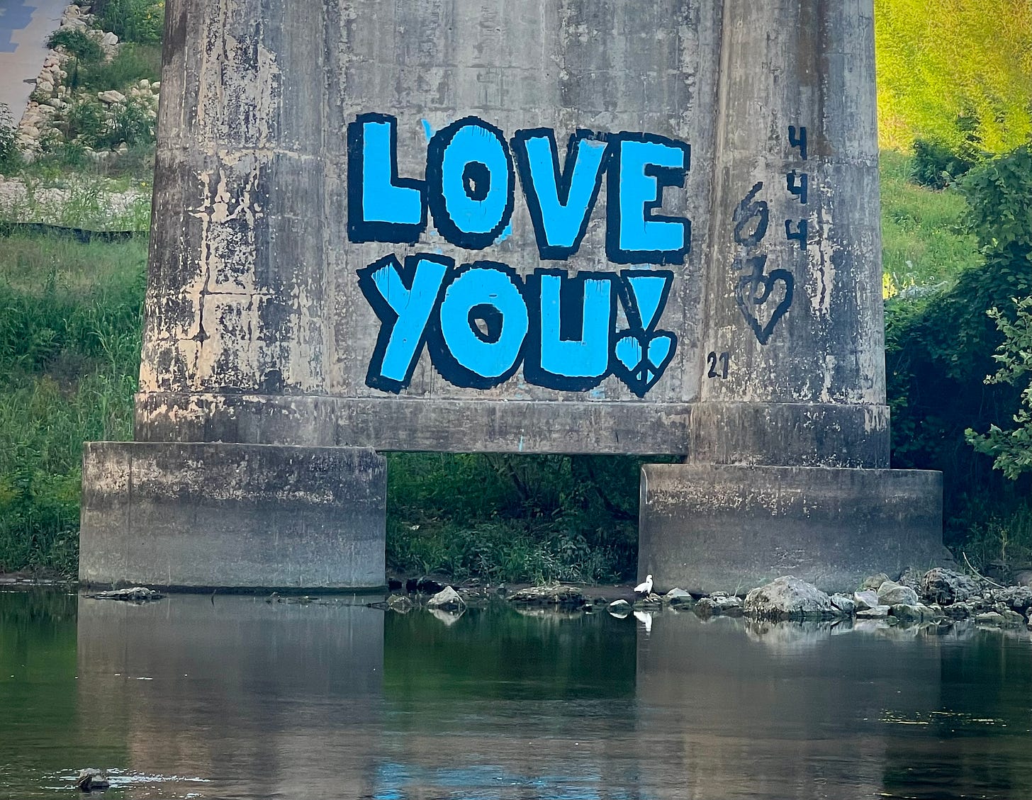 Bridge pillar with LOVE YOU! graffiti and an egret fishing in the river shallows