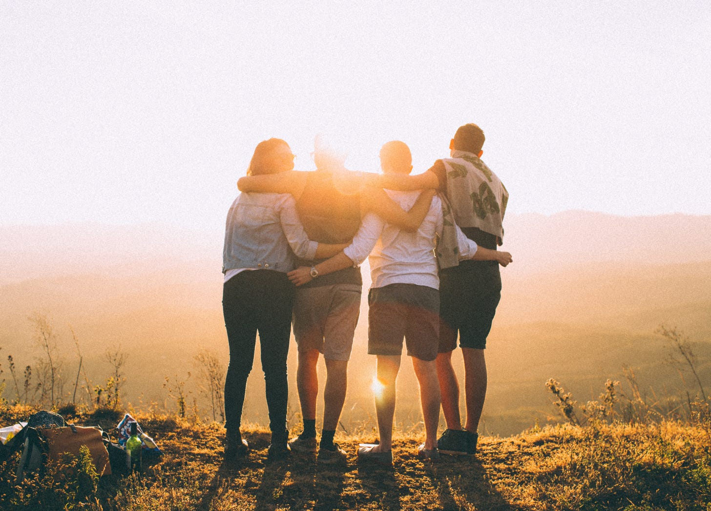 Four people stand arm in arm at sunrise on a scenic overlook, symbolizing community, shared journeys, and the support found in the WaterCooler Chat for corporate dropouts transitioning to self-made success.