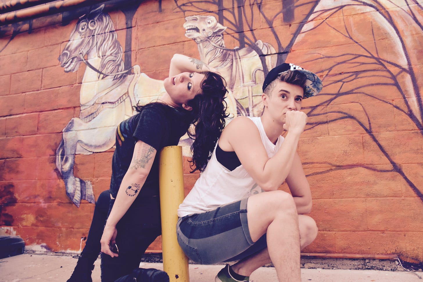 A promo image for the band Damsel Trash shows Emily and Meg in a silly pose in front of a colorful mural.