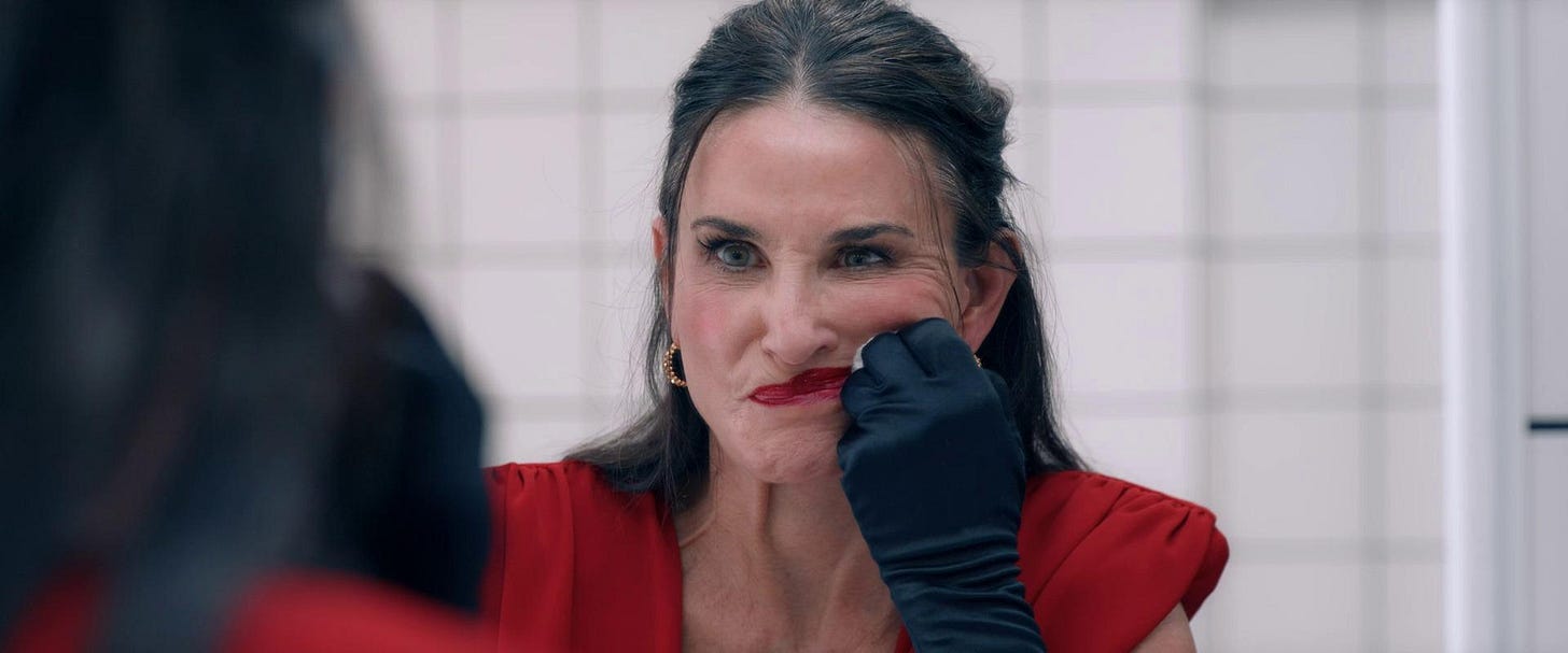 Demi Moore smudges lipstick across her face, looking at herself hatefully in the mirror