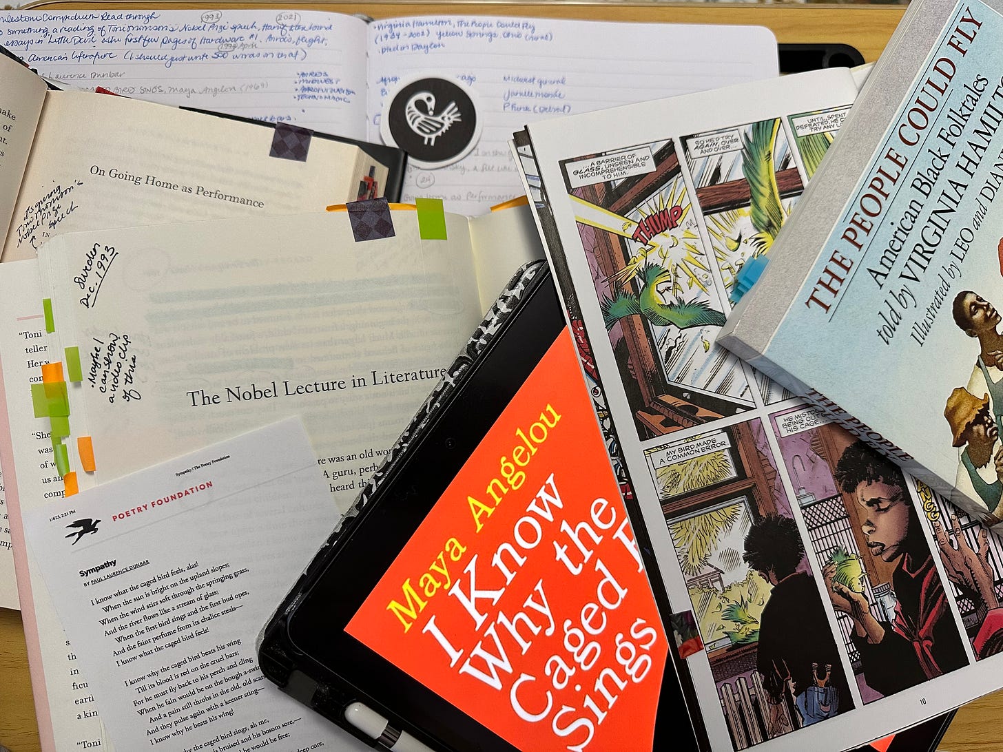 A mess of books and notebooks stacked on top of each other in a pile. Ravynn's handwritten journal, Toni Morrison's the Source of Self-Regard open to her Nobel Lecture in Literature, Hanif Abdurraqib's A Little Devil in America open to "On Going Home as Performance," a copy of Paul Laurence Dunbar's poem "Sympathy," the cover of Maya Angelou's I Know Why The Caged Bird Sings ebook, Milestone Compendium One open to the first pages of Hardware #1, a copy of Virginia Hamilton's The People Could Fly. Most of the books are annotated and tabbed.