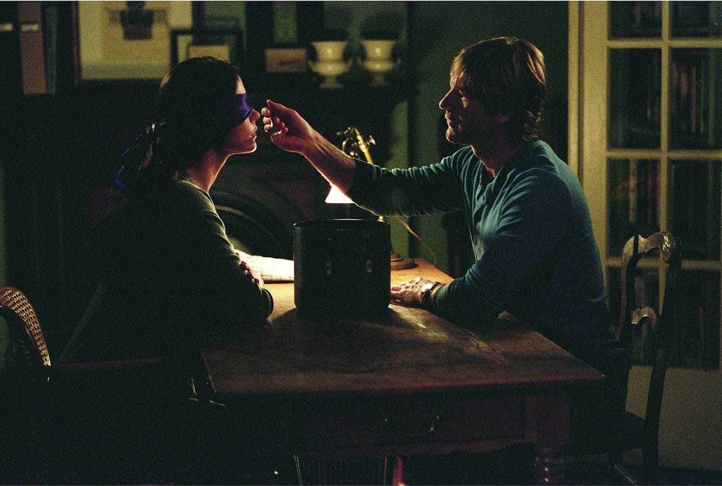 Movie still from No Reservations. A man feeds a blindfolded woman a dessert at a kitchen table.