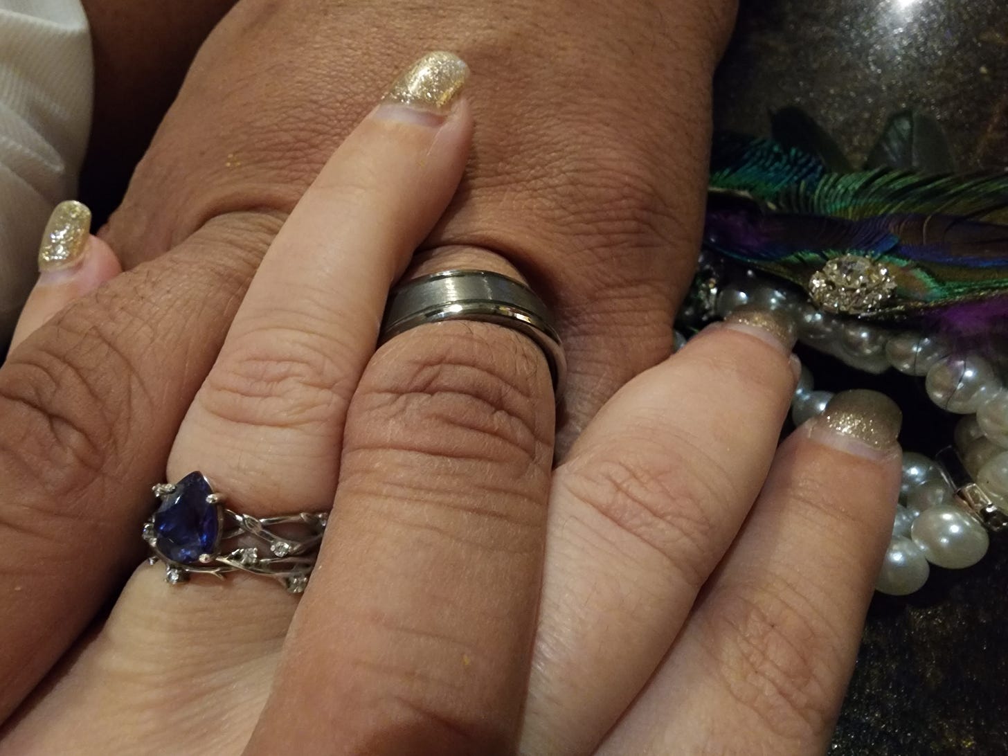 Image of married couple holding hands, focus is on their wedding bands.