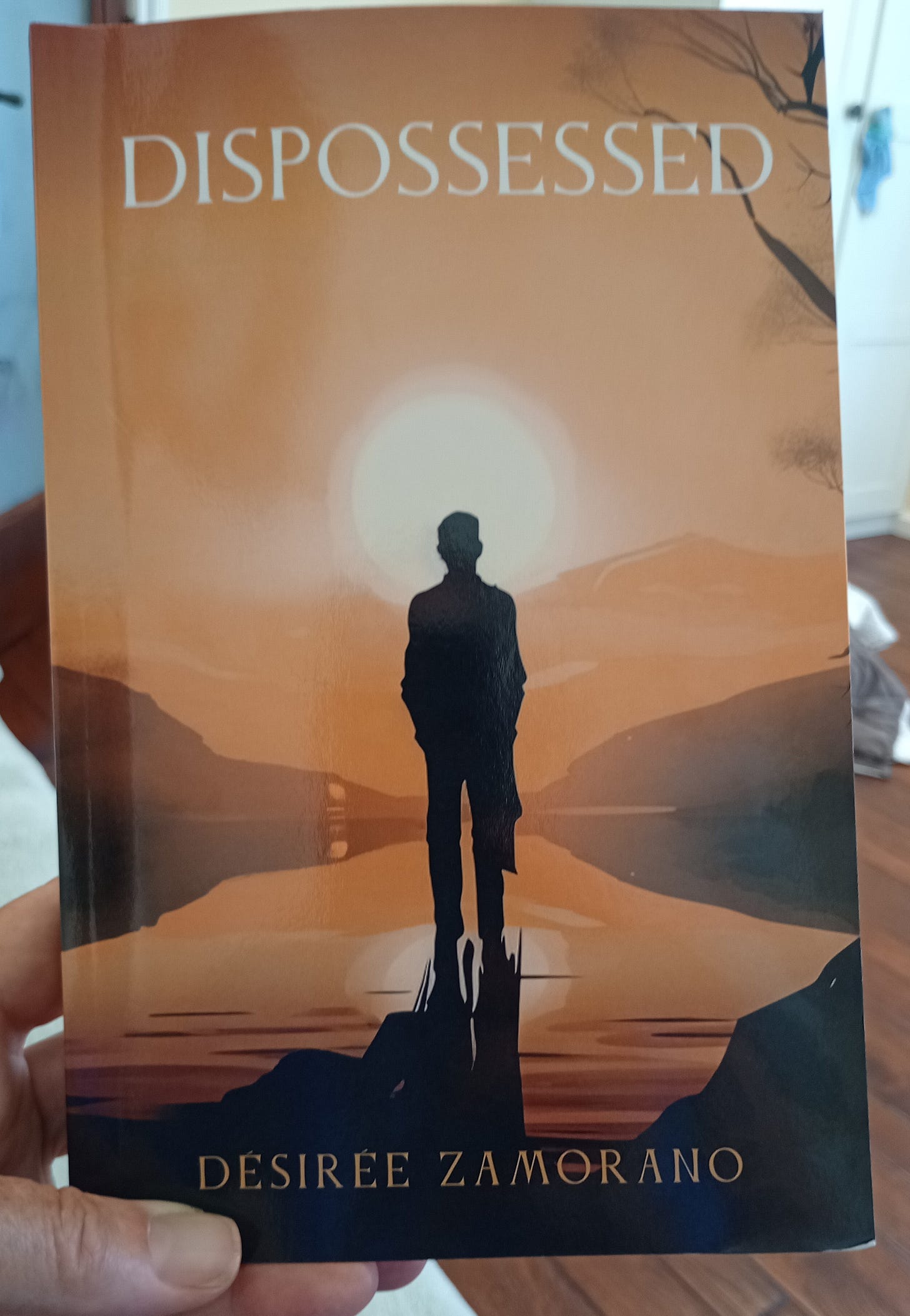 hand holding book with brown cover and the word dispossessed on the front with silhouette of young boy