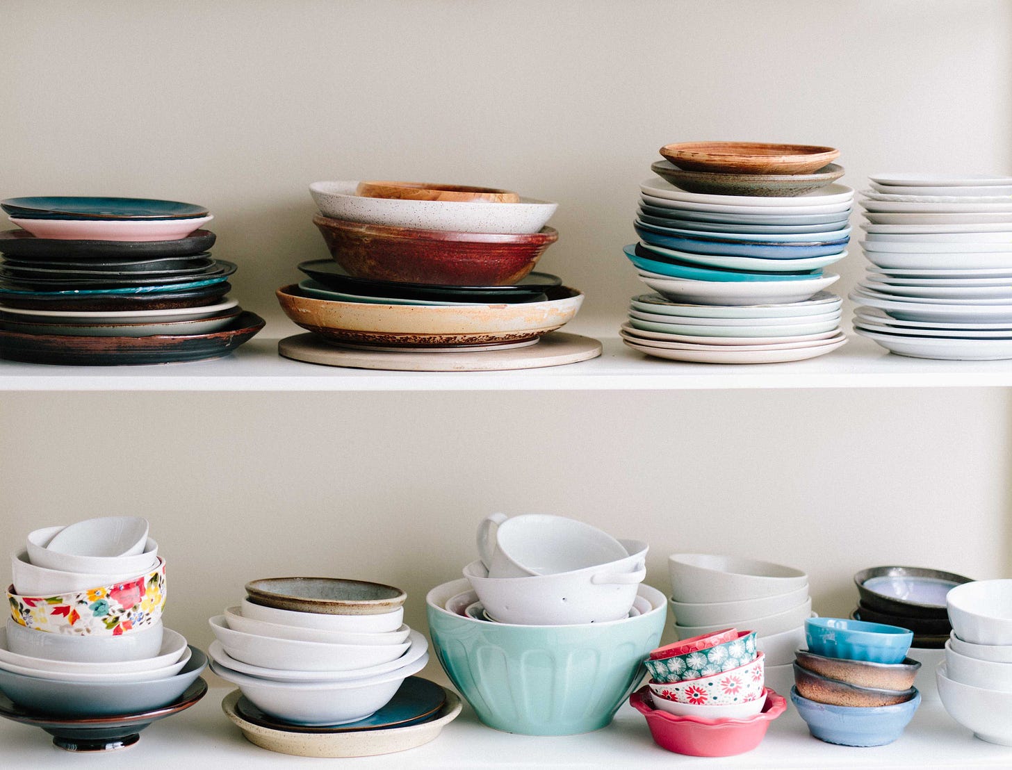 Two shelves of assorted plates and bowls in a variety of colors